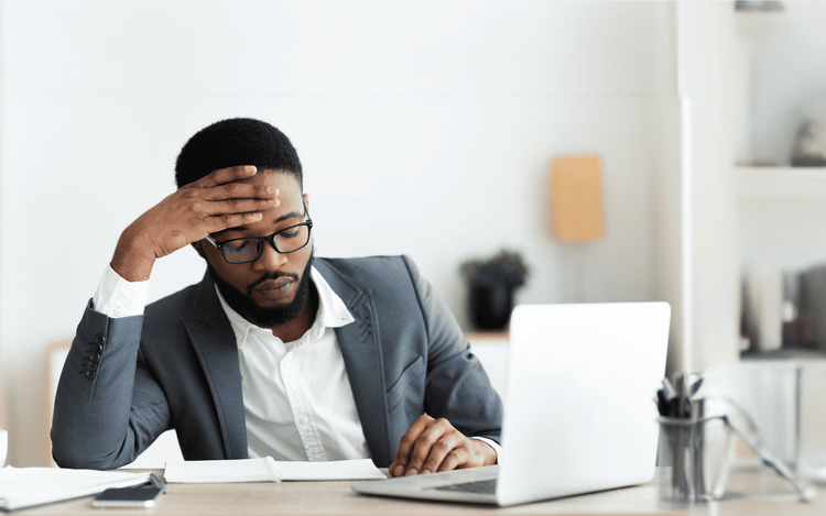Man sitting in front of his laptop with his hand on his head.