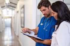 2 doctors are stood in the hallway looking over a patient chart