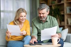 Man and woman looking at a phone screen while holding papers