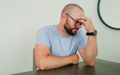 A man sat at a table with his head in one of his hands looking exhausted
