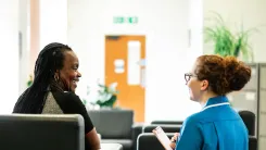 Doctor is kneeling down to speak to her patient who is sitting on a couch