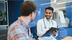 A man is speaking to his doctor while the doctor is smiling at him and taking notes