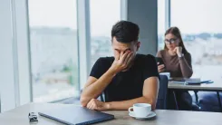 Man is sat at a table and rubbing his eyes