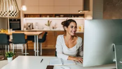 Woman is sat at a desk and smiling at her computer screen