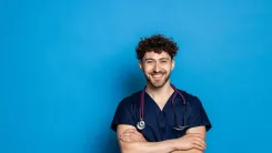 Male medical professional standing and smiling with his arms crossed in front of a blue background